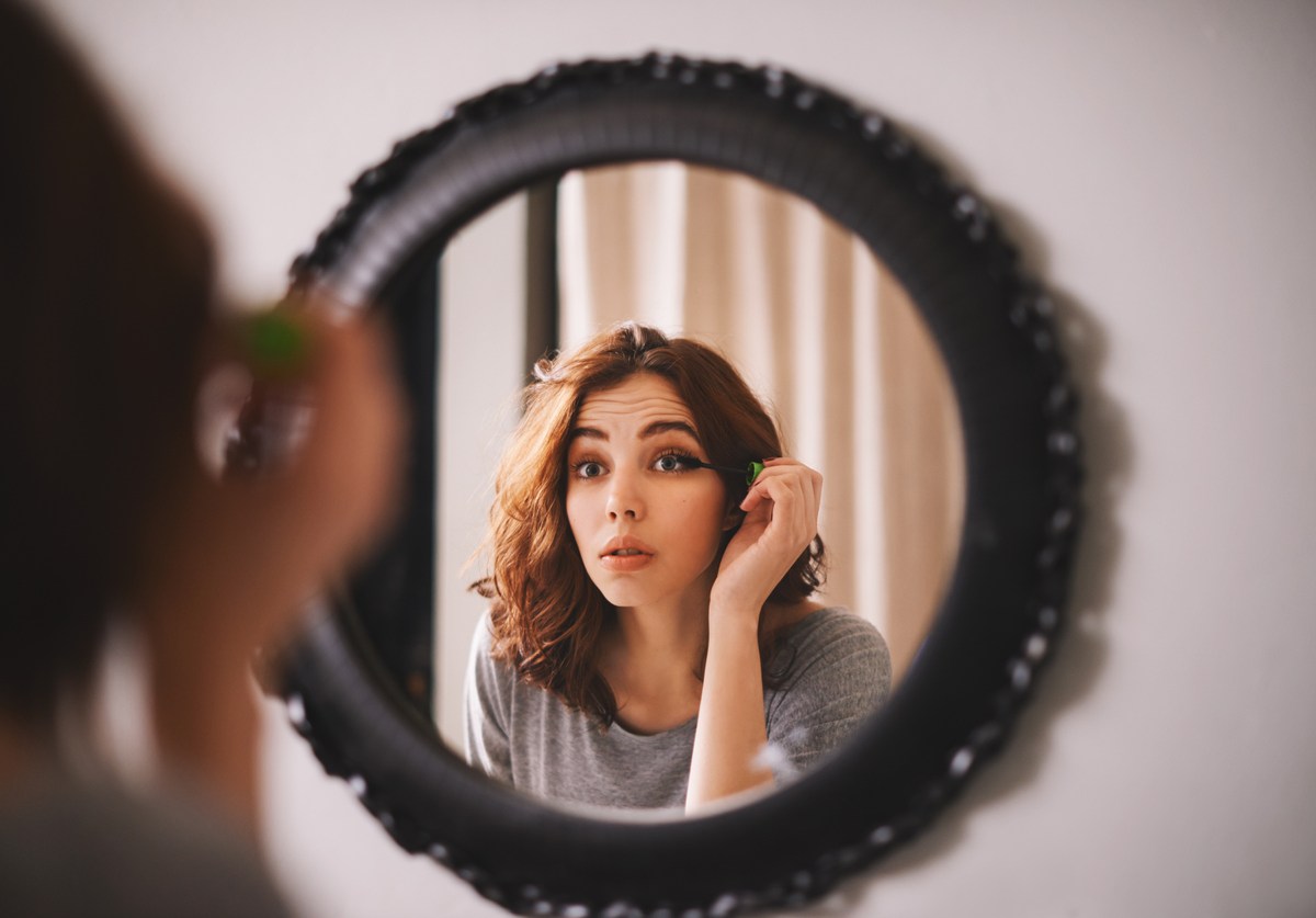 Frau trägt Make Up vor dem Spiegel auf