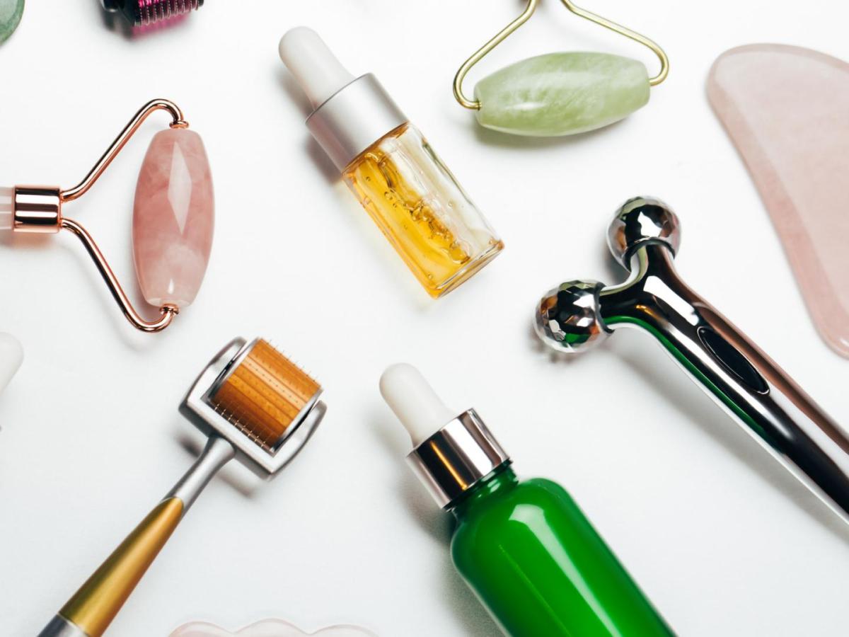 Top view of set of aromatic oils placed amidst various massage rollers and gua sha scraping tools on white background