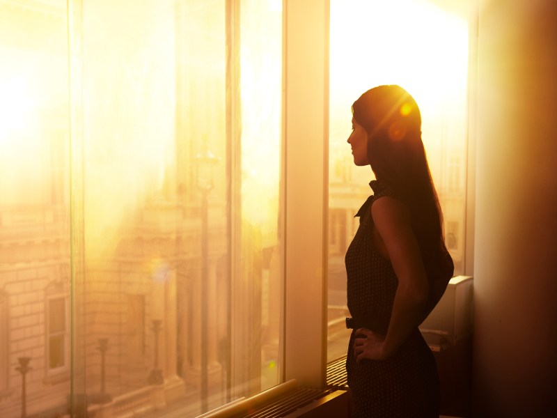 Eine Frau steht im BÃ¼ro vor dem Fenster. Es ist Sonnenuntergangsstimmung.