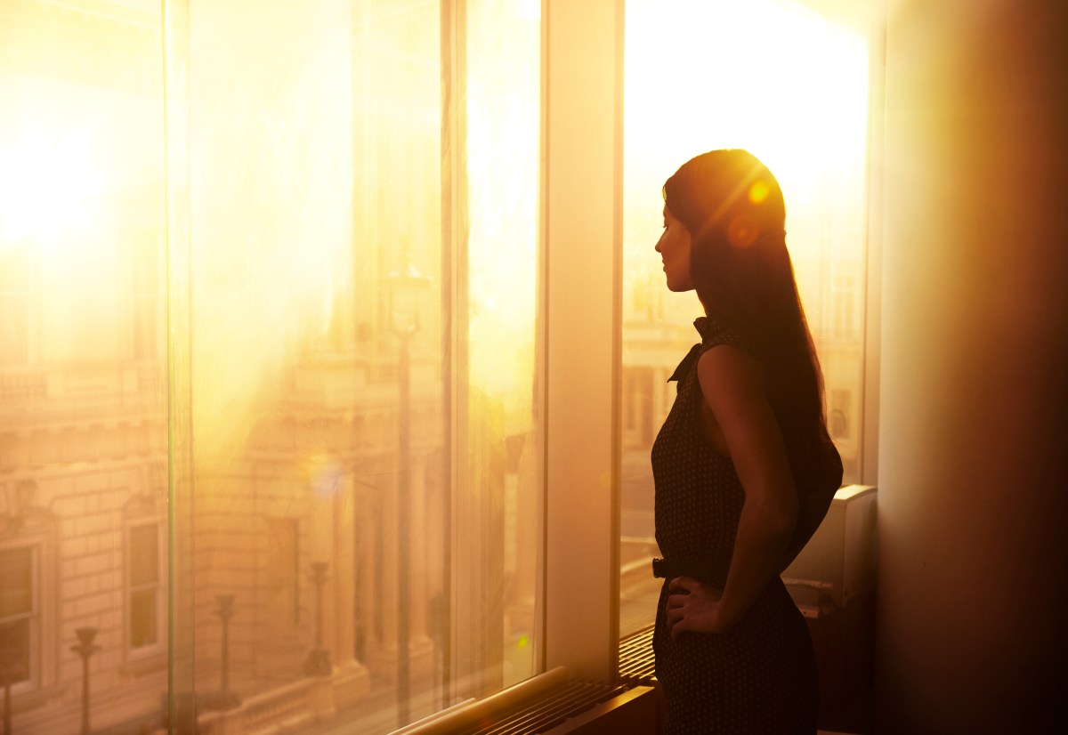 Eine Frau steht im BÃ¼ro vor dem Fenster. Es ist Sonnenuntergangsstimmung.