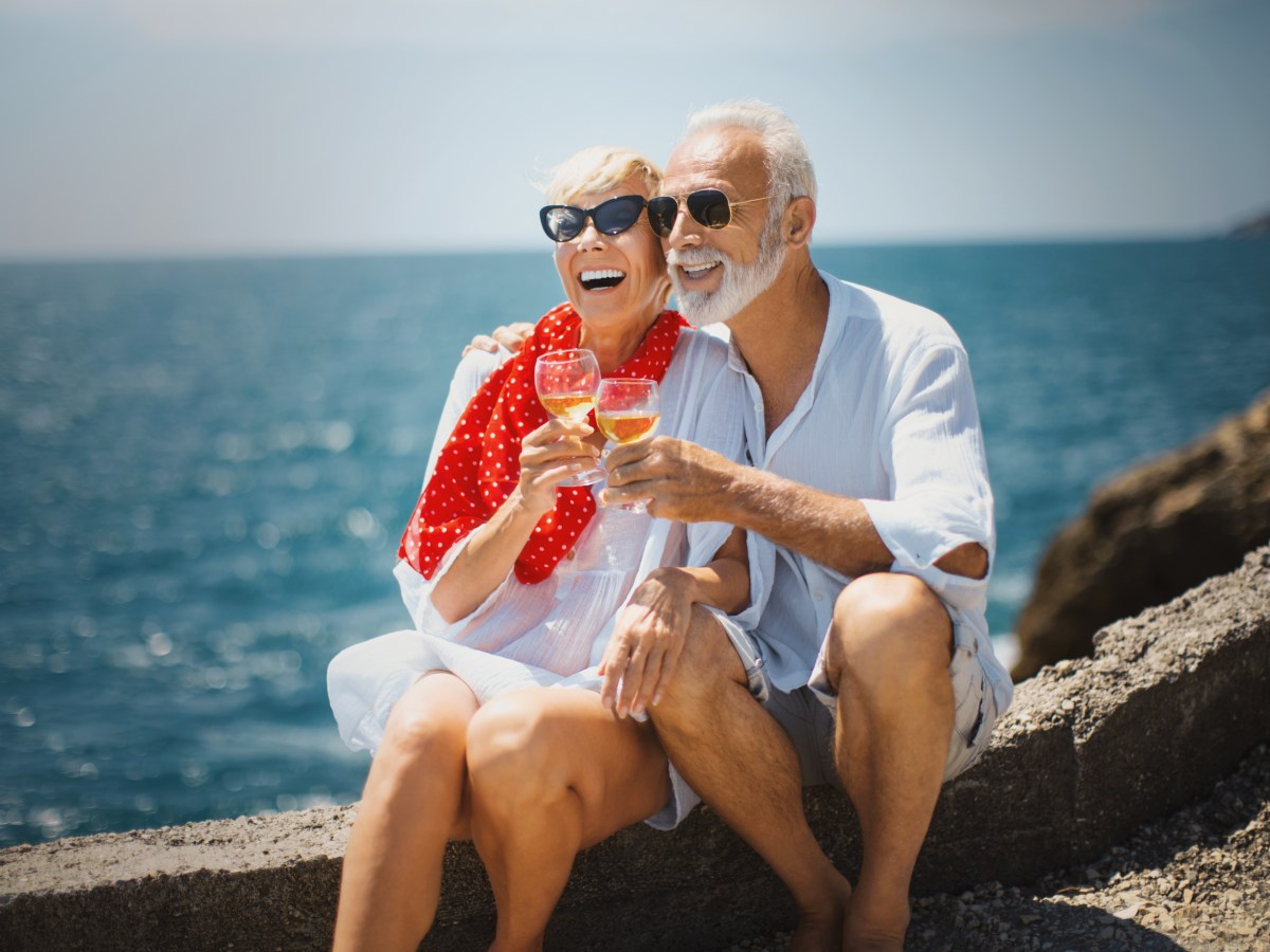 Ein RentnerpÃ¤rchen sitzt am Meer und trinkt Wein.