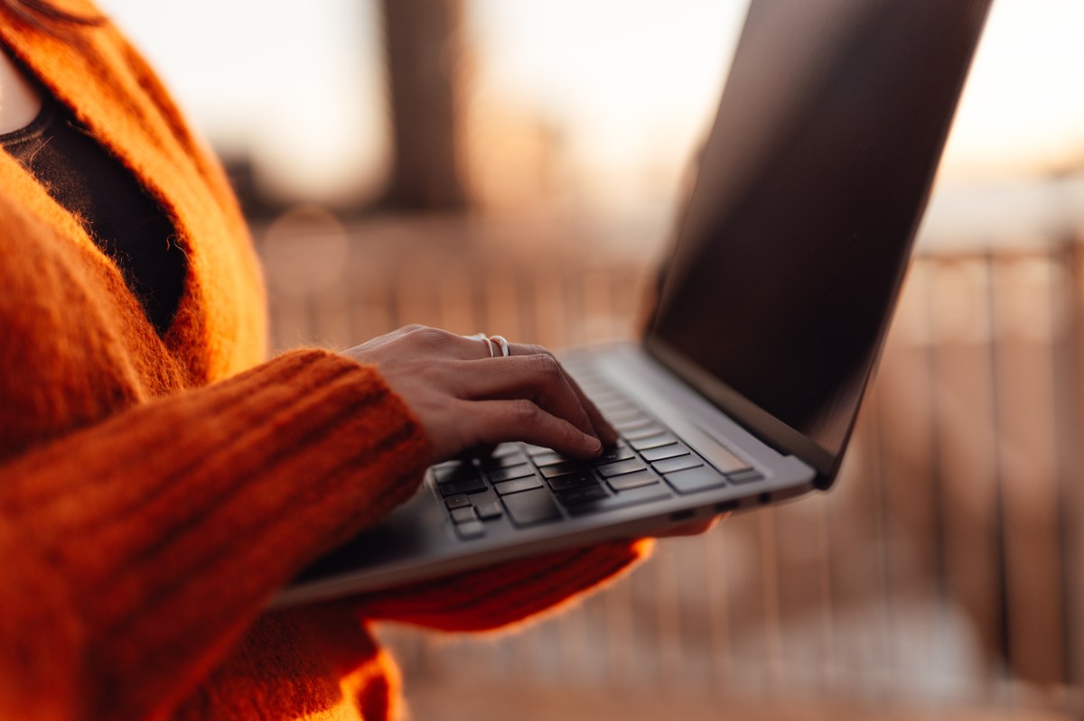 Frau tippt mit der Hand auf einer Laptop-Tastatur in einer AuÃŸenumgebung in der Stadt.