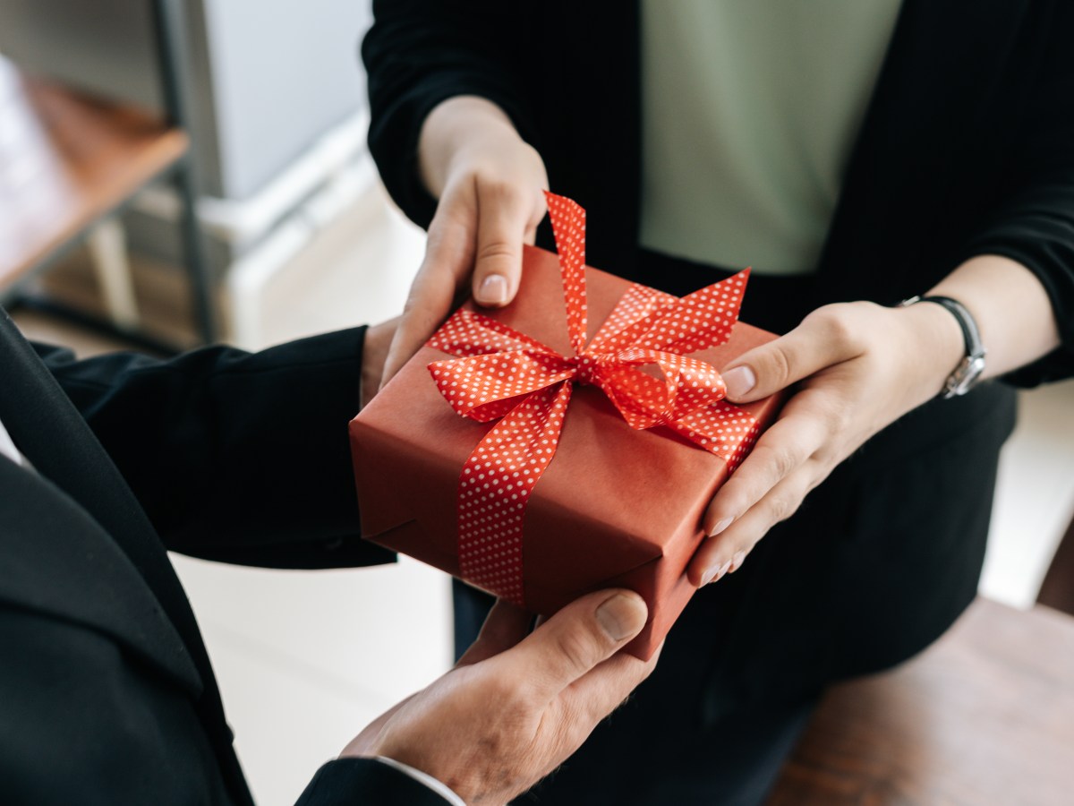 Eine Person Ã¼bergibt ein Geschenk mit roter Schleife.