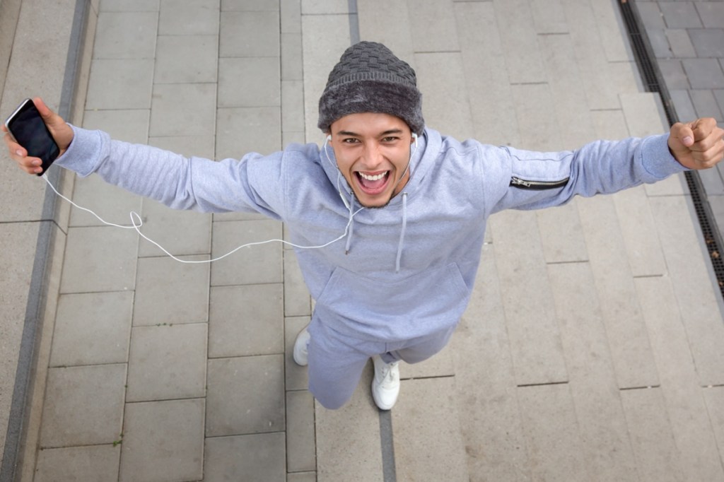 Ein junger Mann im Jogginganzug hält die Arme in die Luft.