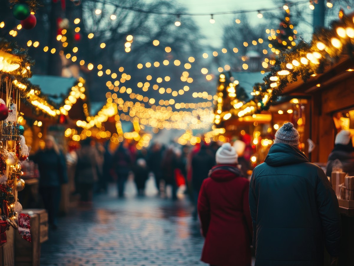 Ein Weihnachtsmarkt am Abend. Die Lichterketten leuchten.