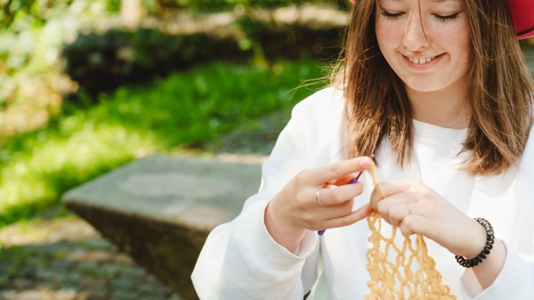 Eine junge Frau strickt im Grünen.