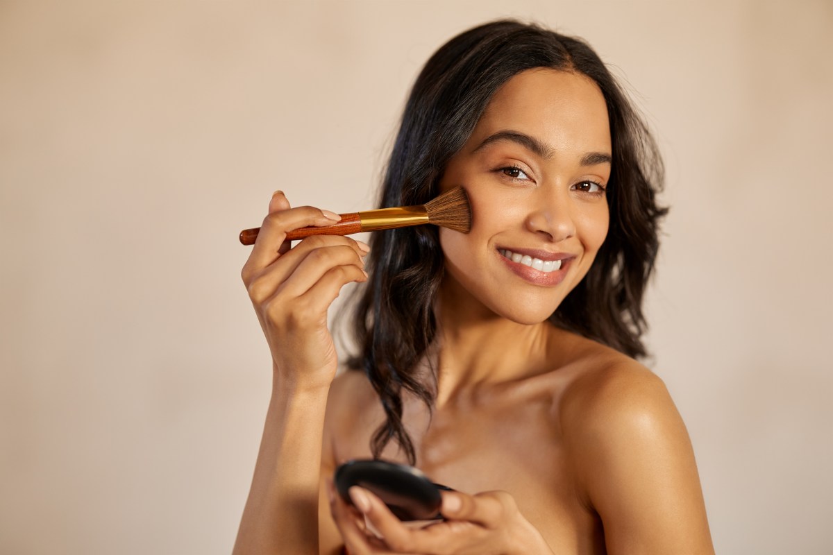 Frau trägt Contouring mit einem Pinsel auf ihre Wangen auf.