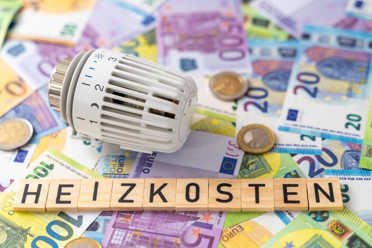 Auf Holzplättchen steht das Wort "Heizkosten": Darunter liegen Geldscheine und daneben ein Thermostat.