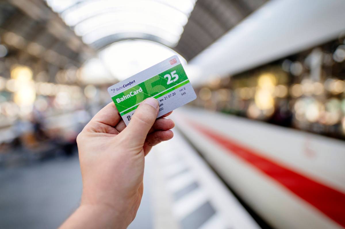 Eine Person hält am Gleis eine BahnCard 25 in der Hand. Im Hintergrund ist ein ICE zu sehen.