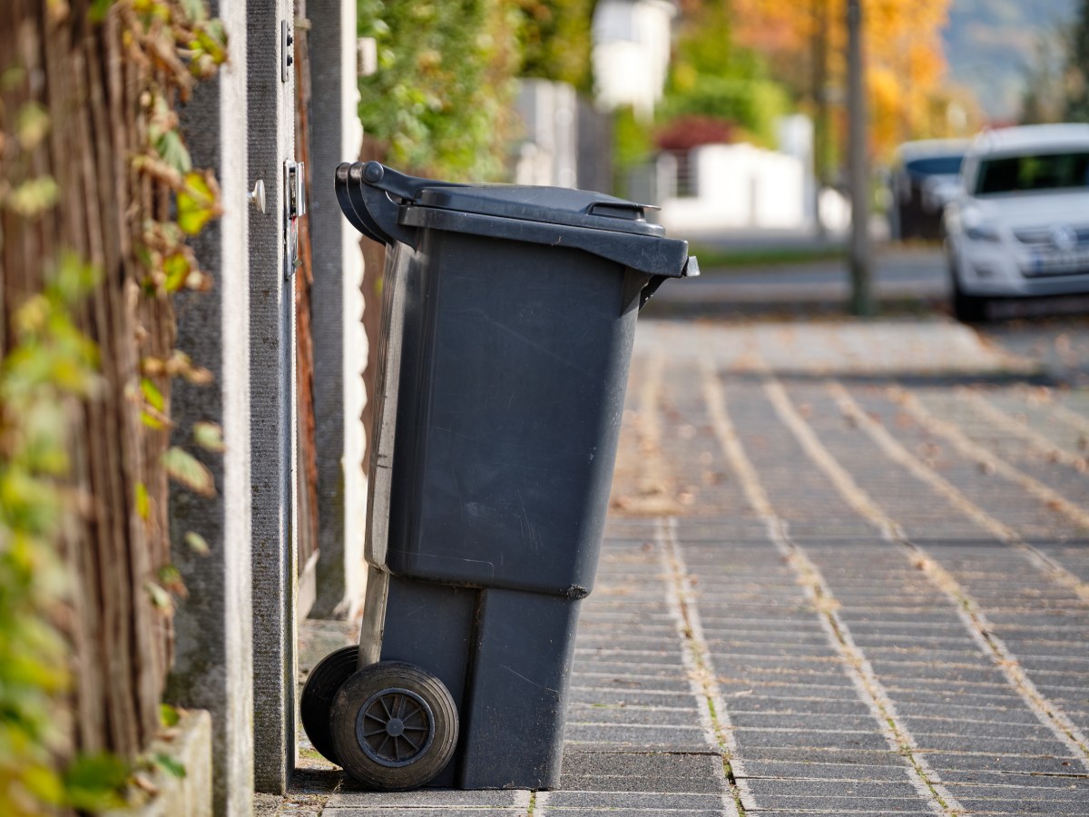 Eine schwarze Mülltonne steht am Straßenrand.