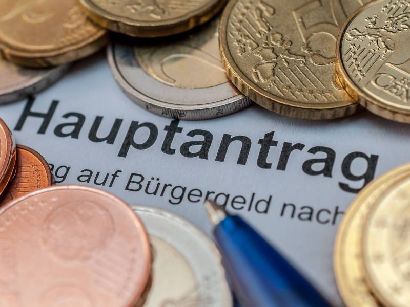 Ein BÃ¼rgergeld-Hauptantrag liegt zwischen vielen Euro-MÃ¼nzen.