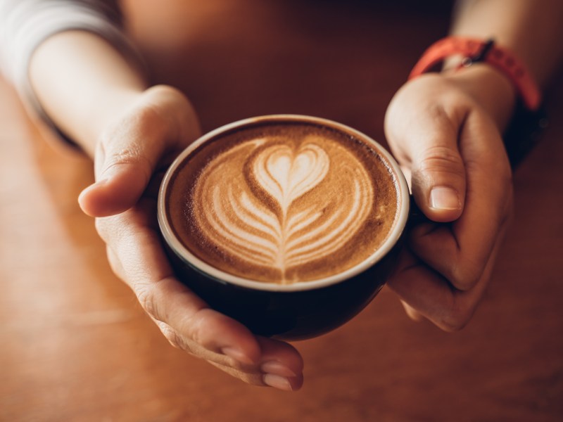 Eine Person hält einen Milchkaffee in der Hand.