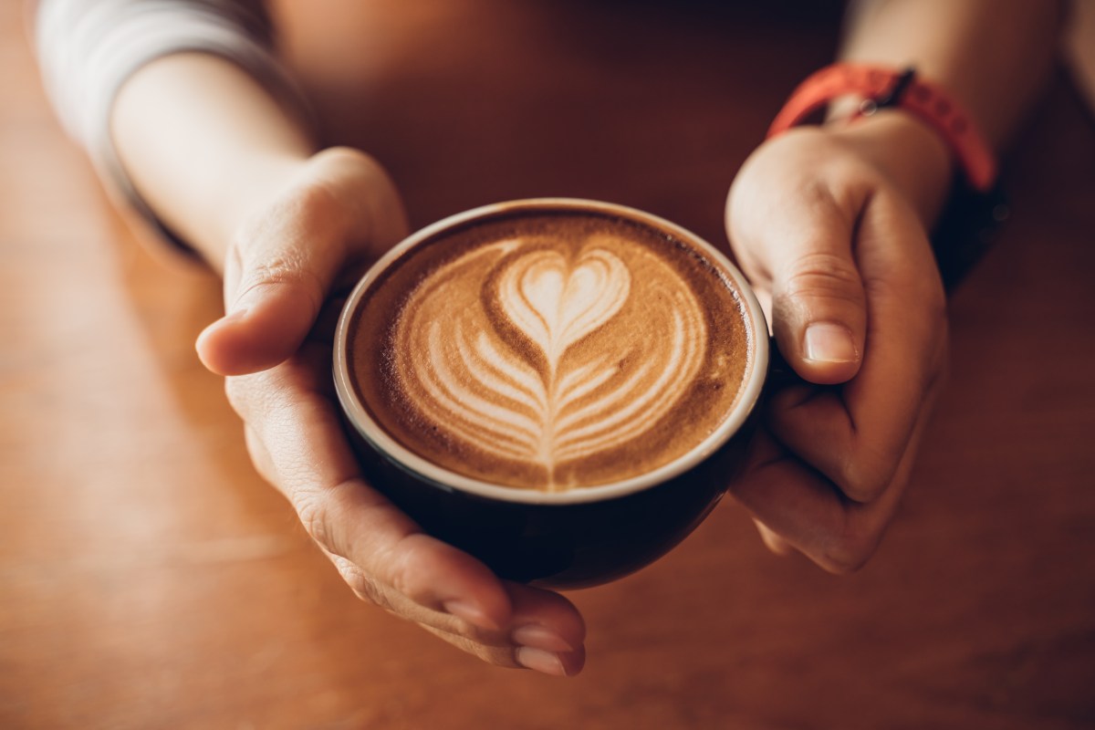 Eine Person hält einen Milchkaffee in der Hand.