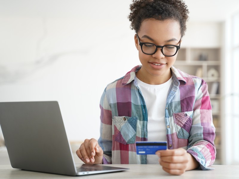 Eine Frau schaut auf ihre Bankkarte. Daneben ist ihr Laptop geöffnet.