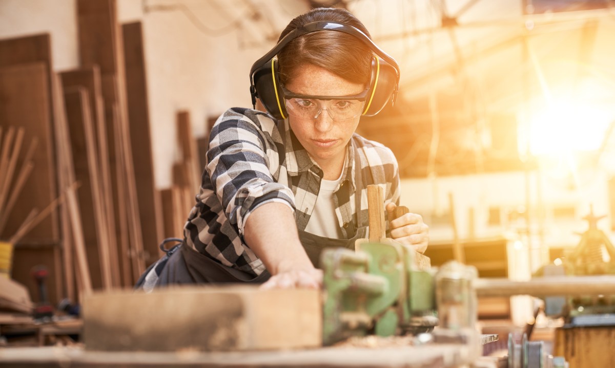 Eine junge Frau arbeitet in der Werkstatt. Sie sägt Holz.