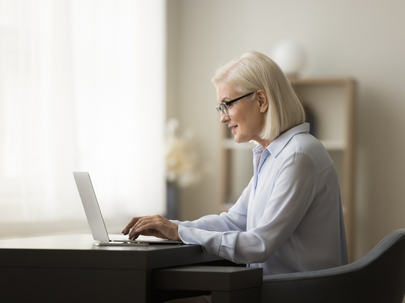 Eine ältere Dame mit weißen Haaren sitzt vor dem Laptop und arbeitet.