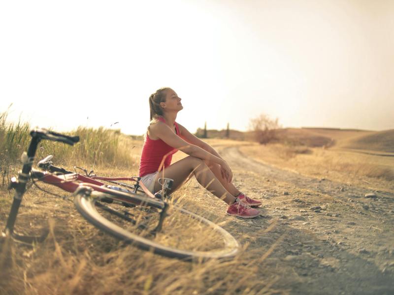 Frau mit Fahrrad macht Pause am Wegrand