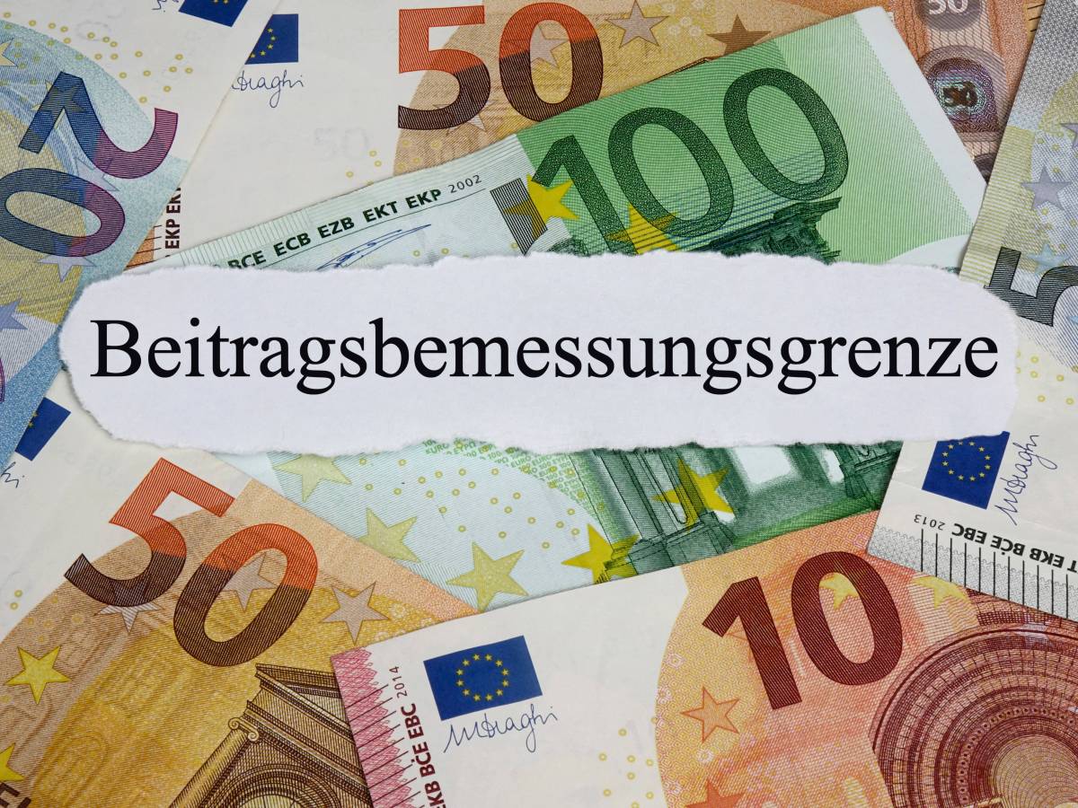 Auf einem weißen Zettel steht das Wort "Beitragsbemessungsgrenze". Darunter liegen Geldscheine.