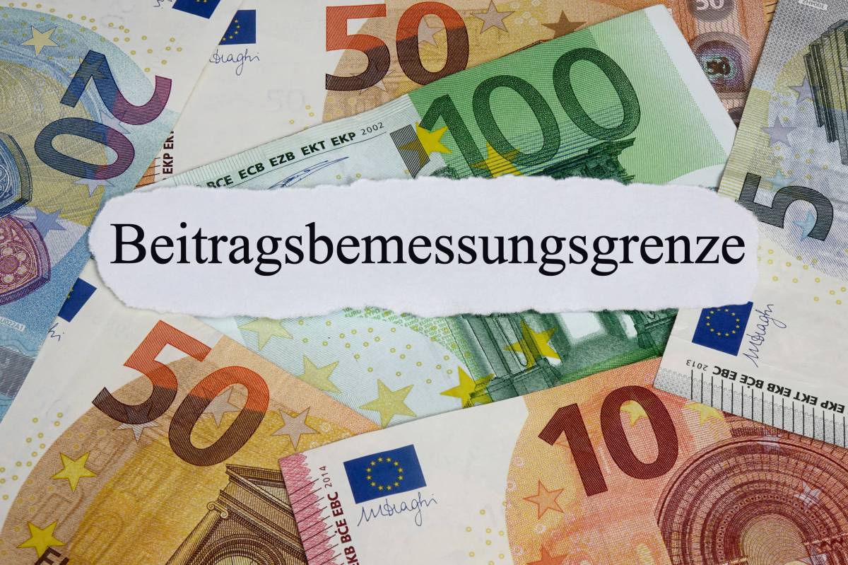 Auf einem weißen Zettel steht das Wort "Beitragsbemessungsgrenze". Darunter liegen Geldscheine.