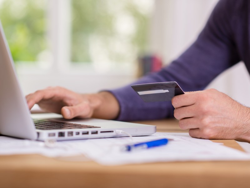 Eine Person sitzt am Laptop und hält eine Bankkarte in der Hand.