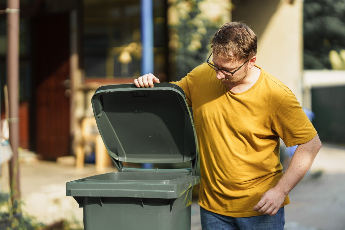 Eine Mann schaut in eine grüne Mülltonne.