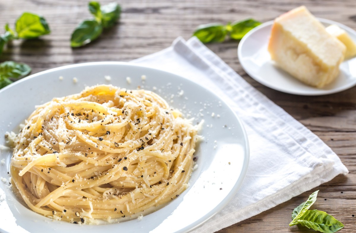 Pasta Cacio e Pepe auf einem weißen Teller, daneben ein Stück Pecorino.