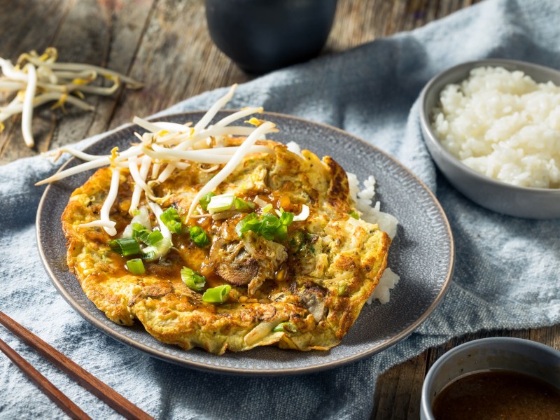 Teller mit Egg Foo Yung und einer Schale Reis auf Tischdecke