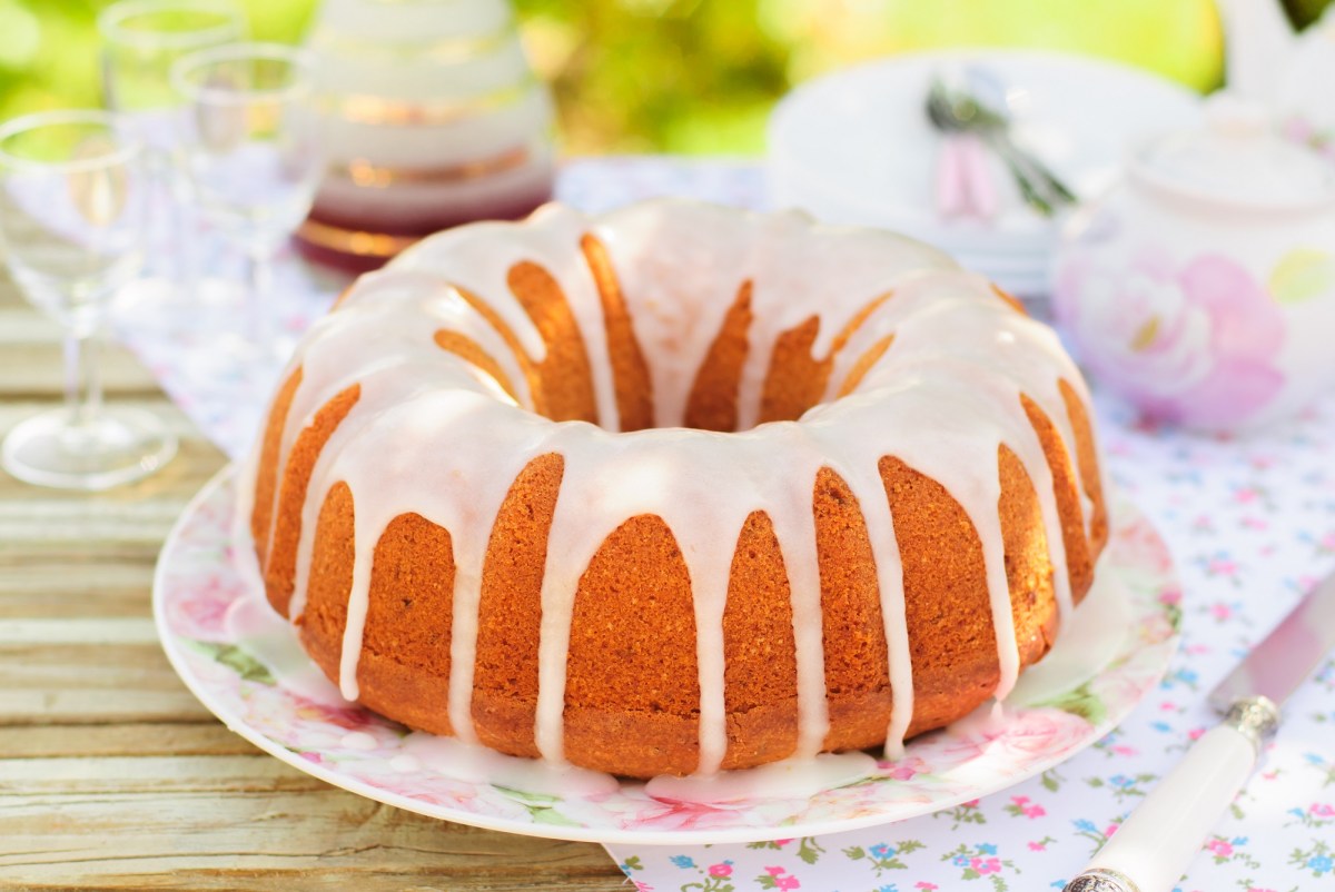 Ein Eierlikörkuchen mit Guss auf einem Blumenteller. Drum herum sind Blumenservietten und Sonnenlicht fällt auf den Kuchen.