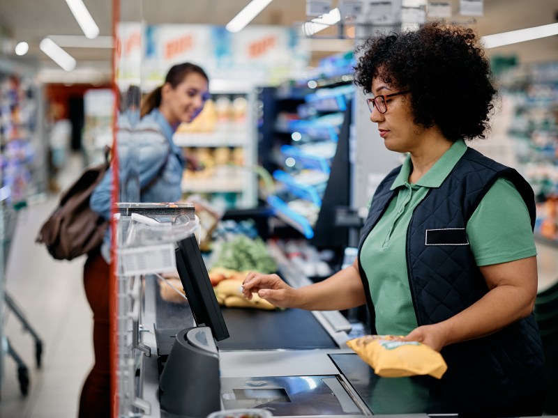 Eine Frau sitzt in einem Supermarkt an der Kasse und scannt Lebensmittel.