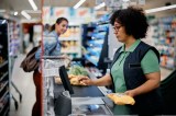 Eine Frau sitzt in einem Supermarkt an der Kasse und scannt Lebensmittel.