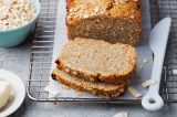 angeschnittenes Haferflocken-Quark-Brot auf einem Brett, daneben eine SchÃ¼ssel Haferflocken und ein Messer.