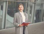 Eine junge Frau steht mit Bewerbungsunterlagen vor einem Bürogebäude.