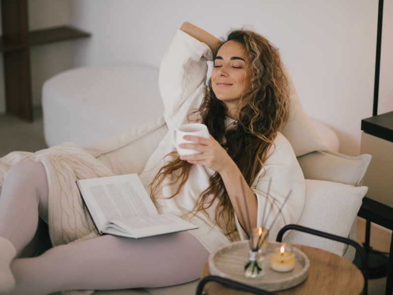 Frau liegt mit einer Decke und einem Buch auf dem Sofa