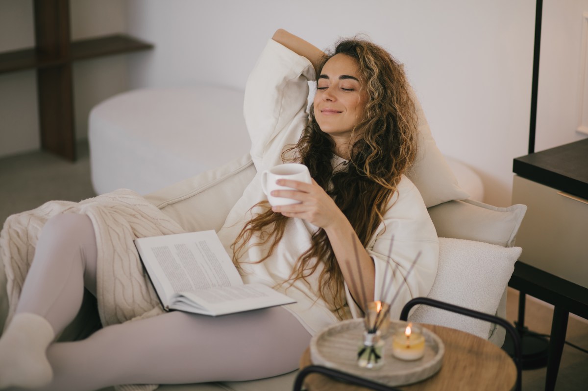 Frau liegt mit einer Decke und einem Buch auf dem Sofa