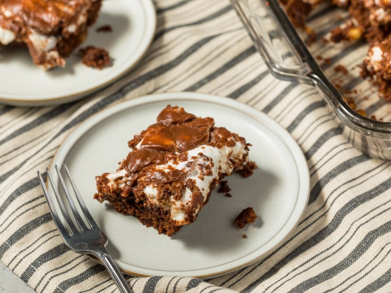 Ein Stück Mississippi Mud Cake auf einem weißen Teller. Daneben steht der Rest des Kuchens.