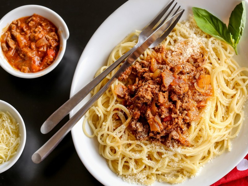 Teller mit One-Pot-Pasta à la bolognese auf holzigem Untergrund