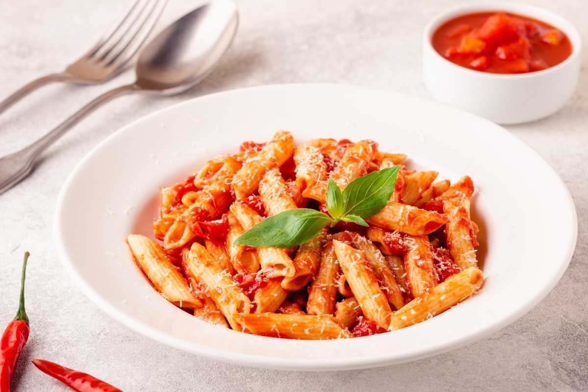 Ein Teller Penne allâ€™arrabbiata. Daneben steht ein SchÃ¤lchen mit Tomaten und es liegt Besteck links vom Teller.