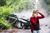 Frau steht vor einem kaputten Auto nach Unfall