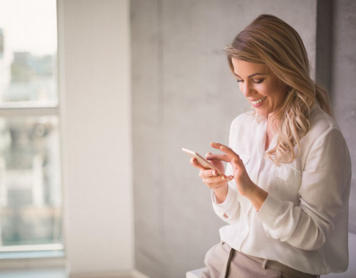 Eine Frau lehnt an der Wand und schaut auf ihr Handy.