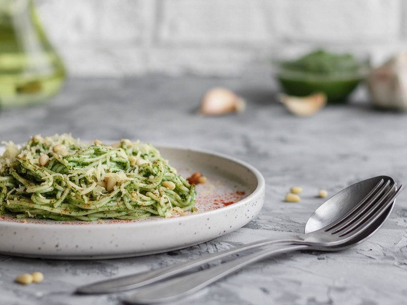 Ein Teller Zucchini-Avocado-Pasta garniert mit Pinienkernen und Parmesan, daneben ein LÃ¶ffel.