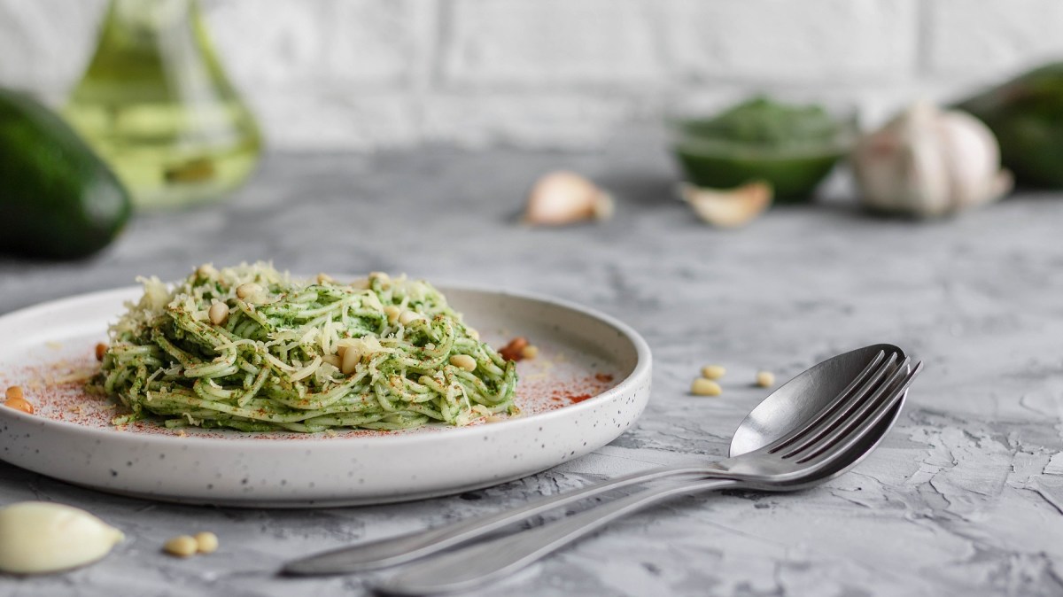 Ein Teller Zucchini-Avocado-Pasta garniert mit Pinienkernen und Parmesan, daneben ein LÃ¶ffel.