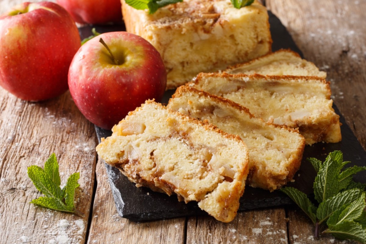 Mehrere Stücke Apfelbrot, die gefächert vor dem restlichen Kuchen liegen. Daneben zwei Äpfel.