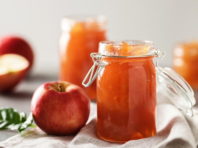 Drei Gläser Apfelgelee und frische Äpfel