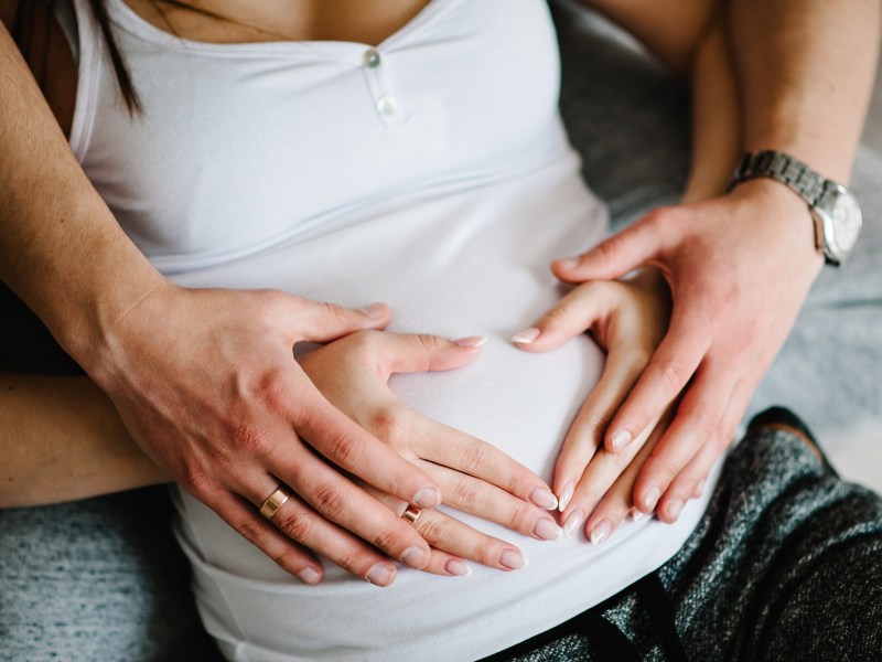 Ausgeschnittenes Bild eines Mannes, der den Bauch seiner schwangeren Frau hält.