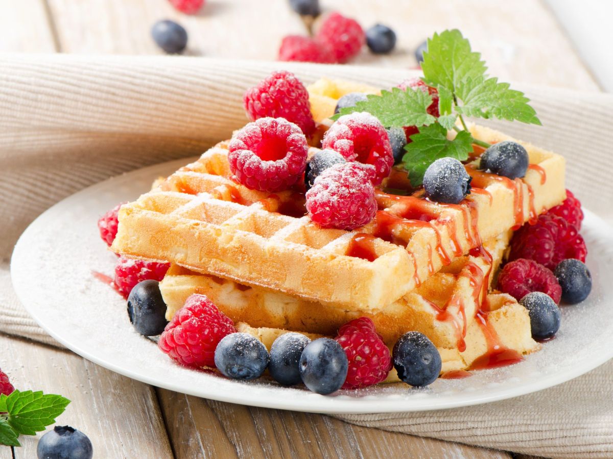 Fantakuchen-Waffeln, auf einem Teller gestapelt. Frische Beeren und ein MinzeblÃ¤ttchen dienen als Deko.