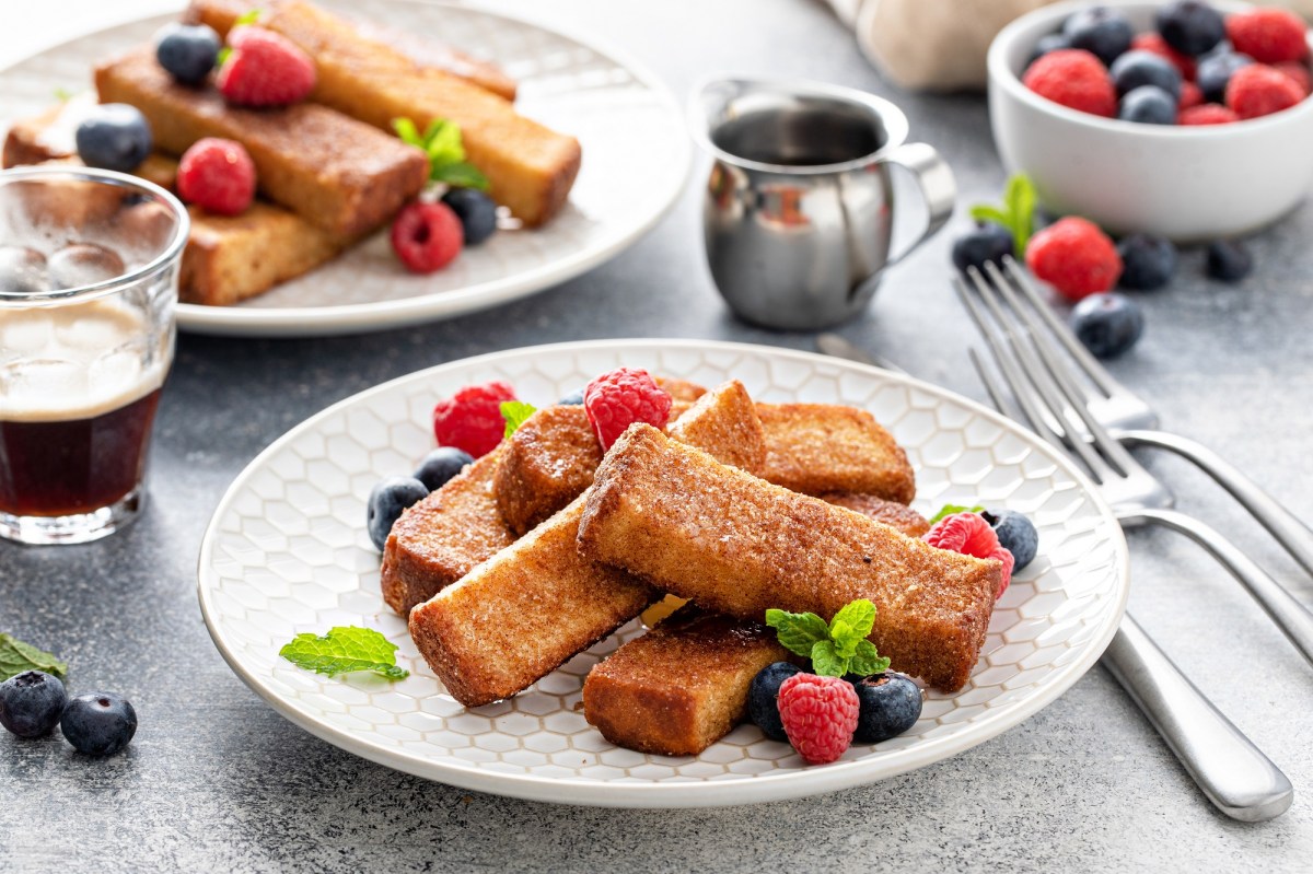 French-Toast-Stangen auf zwei Tellern, garniert mit Beeren, daneben Besteck.