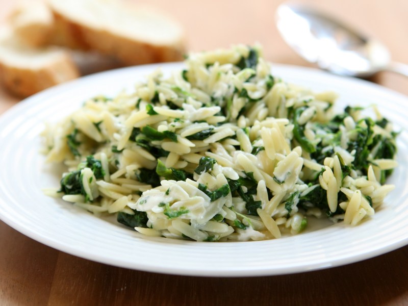 Ein Teller Orzo-Nudeln mit Spinat und Feta, daneben ein Löffel und Baguettescheiben.