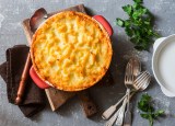 Shepherd's Pie mit Linsen und Kartoffelpüree in runder Auflaufform in der Draufsicht, daneben Besteck und Kräuter.