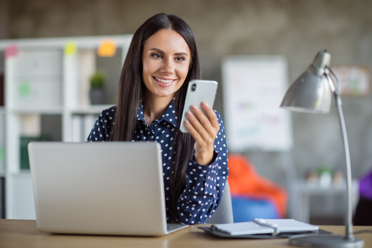 Eine Frau sitzt an ihrem Arbeitsplatz und schaut auf ihr Handy.