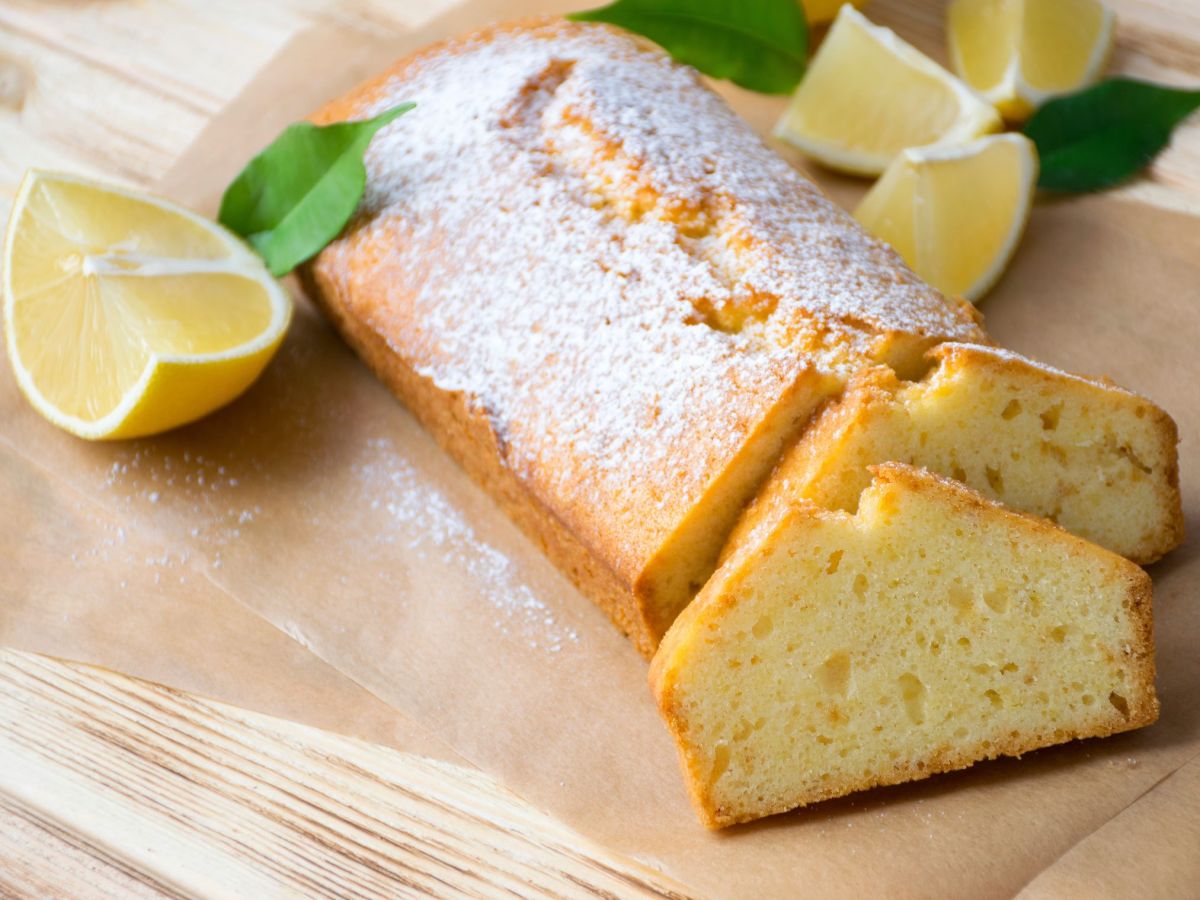 Aufgeschnittener veganer Zitronenkuchen, serviert auf einem Brett. Eine aufgeschnittene Zitrone und MinzblÃ¤tter liegen als Deko neben dem Kuchen.